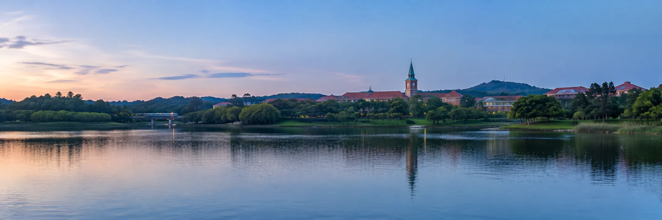 Songshan Lake in Dongguan at dusk, red-roofed buildings and a green spire reflected in the water.